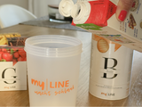 Eine Dose myLINE Basis, verschiedene myLINE Geschmacksvariationen und ein Shaker, in den Milch gefüllt wird