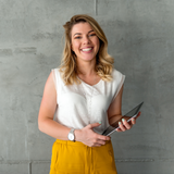 Eine blonde Frau mit gelber Hose steht vor einer grauen Wand und hält ein I-Pad in der Hand mit gratis Ernährungs- und Abnehmtipps von myLINE.